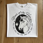 White t-shirt with a black horse graphic and text on a wooden surface